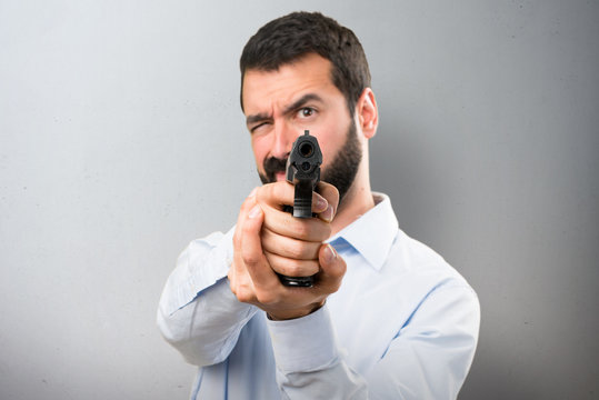 Handsome man with beard shooting with a pistol on textured background