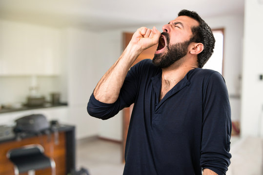 Handsome man with beard yawning inside house