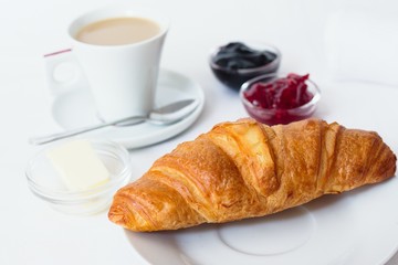 Fresh french croissant served with jams, butter and a cup of coffee with milk
