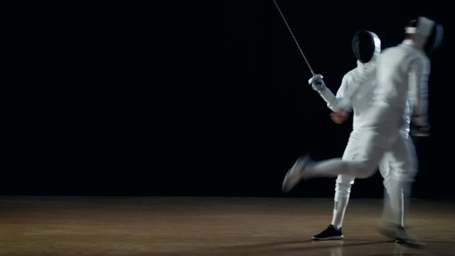Two Professional Fencers Show Masterful Swordsmanship in their Foil Fight. One Performs Beautiful Fleche Attack. Shot Isolated on Black Background.