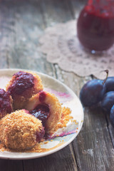 Plum dumplings, plums and plum sauce on wooden background