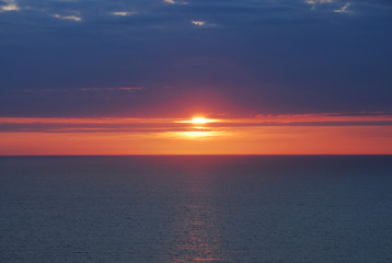 Beautiful Red and Blue Sunset or Sunrise horizon over the Ocean, sun peering through the cloudy sky