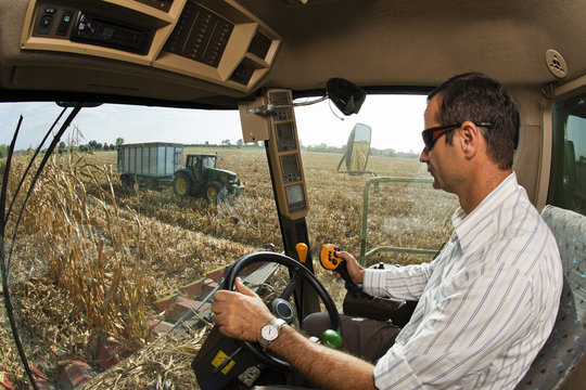 Driver of the combine, observes from the driving position, the tractor with the trailer on the field of corn threshed