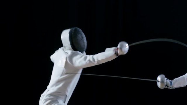 Two Professional Fully Equipped Fencers Expertly Fight with Foils. One Lunges and Wins, He Takes of His Mask in Winning Glory. Shot in Slow Motion and on Isolated Black Background. 