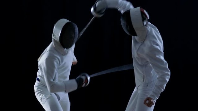 Two Professional Fully Equipped Fencers Expertly Fight with Foils. They Attack, Defend, Leap and Thrust and Lunge. Shot in Slow Motion and on Isolated Black Background. 
