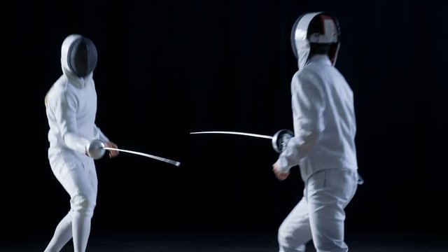 Two Professional Fully Equipped Fencers Expertly Fight with Foils. They Attack, Defend, Leap, Thrust and Lunge. Shot in Slow Motion and on Isolated Black Background. 