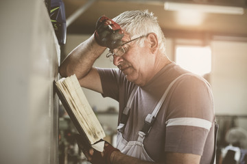 Senior man in workshop. Worried  man reading his planner.