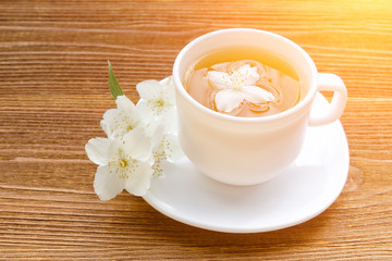 White mug of tea with jasmine on a wooden table. Close up, sunlight