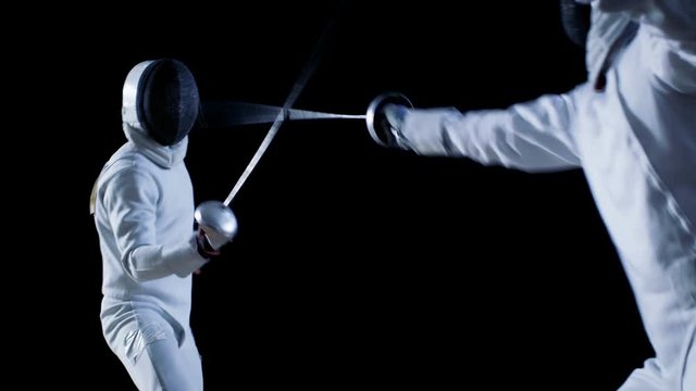 Two Professional Fully Equipped Fencers Expertly Fight with Foils. They Attack, Defend, Leap, Thrust and Lunge. Shot in Slow Motion and on Isolated Black Background. 