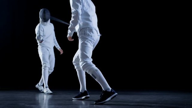 Two Professional Fully Equipped Fencers Expertly Fight with Foils. They Attack, Defend, Leap, Thrust and Lunge. Shot in Slow Motion and on Isolated Black Background.  