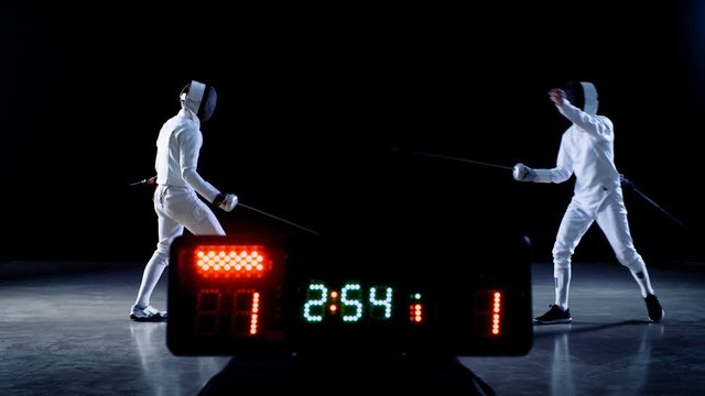 On the Championship Two Professional Fully Equipped Fencers Expertly Fight with Foils while Scoreboard Keeps the Scores of Hits. They Attack, Defend, Leap, Thrust and Lunge. 