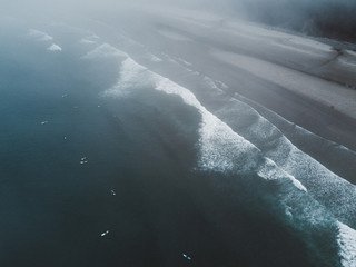 Aerial shot of surfers on beach with forest behind in fog - 171754364