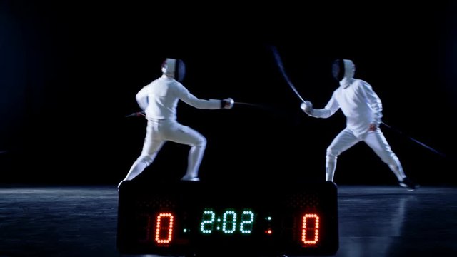 On the Championship Two Professional Fully Equipped Fencers Expertly Fight with Foils while Scoreboard Shows Hits. They Attack, Defend, Leap, Thrust and Lunge. Shot Isolated on Black Background. 