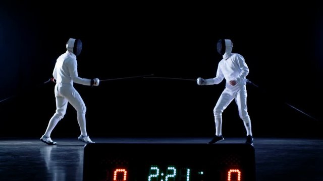 On the Championship Two Professional Fully Equipped Fencers Expertly Fight with Foils while Scoreboard Shows Hits. They Attack, Defend, Leap, Thrust and Lunge. Shot Isolated on Black Background. 