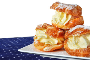 Cream puff with vanilla custard sprinkled with powdered sugar on white plate over napkin isolated on white background.