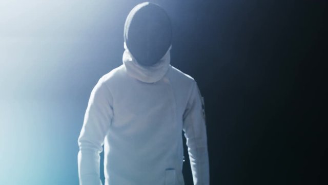 Portrait Shot of a Fully Equipped Skilled Fencer Training with a Foil in a Spotlight while Darkness is Around Himl. He Practices Attack, defense,  Leap, Thrust and Lunge.