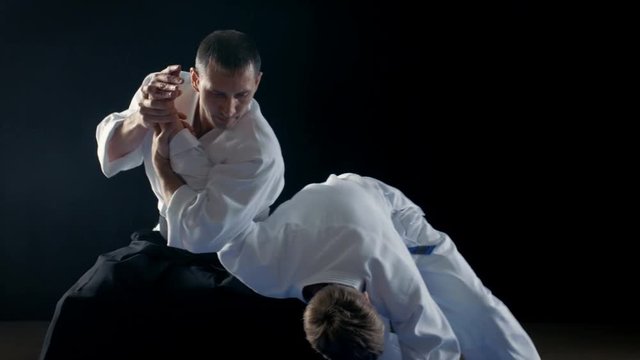 Martial Arts Aikido Master Wearing Hakamas Teaches Young Student How to Defend Himself Against an Attack. Hand Grab Technique. Shot Isolated on Black Background. 
