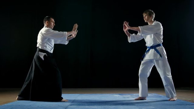 Martial Arts Master Wearing Traditional Samurai Hakamas and His Young Student Bow to Each Other and Take Battle Stance. Shot Isolated on Black Background and in Slow Motion. 