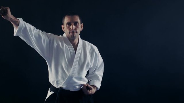Portrait Shot of the Aikido Master Wearing Traditional Samurai Hakama Clothes Takes His Japanese Sword out of Scabbard and Swings with It. He's in the Spotlight Darkness Surrounds Him. 