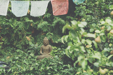 Buddha sculpture on green nature and buddhist prayer flags