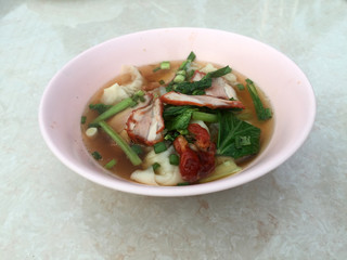 Wonton soup and Barbecued red pork with green Vegetable in the pink bowl on the white marble table.