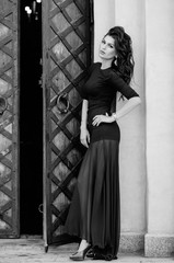 attractive brunette in black dress stands in full growth on building background. Fashion photo. Black and white photo