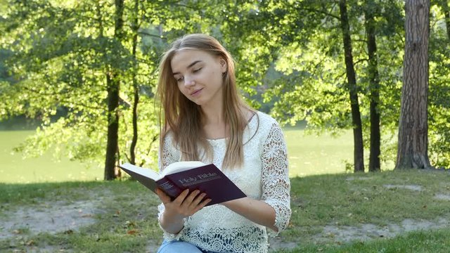 4k. Attractive smiling girl reads  Bible in park. Christian team shot