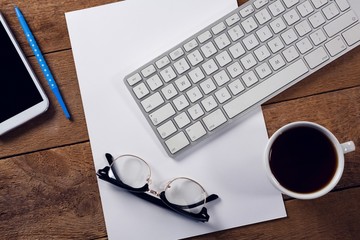 Black coffee, keyboard, spectacles and paper on wooden table