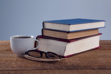 Spectacles, black coffee and book stack on wooden table