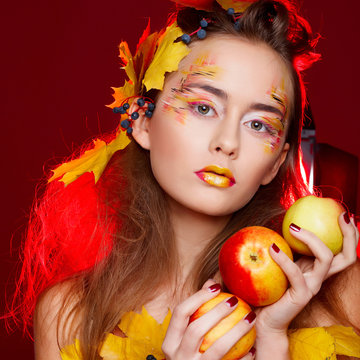 Beautiful young woman with autumn make up holding apples in her hands posing in studio over red background. Fashion concept.