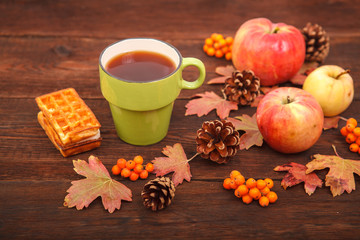 autumn composition. still life. berries of mountain ash, pine cones, fallen leaves and a cup of tea on a background of wood.