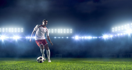 Soccer player kicks the ball on the soccer stadium. He wear unbranded sports clothes. Stadium and...