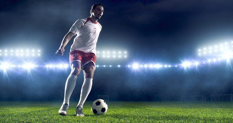 Soccer player kicks the ball on the soccer stadium. He wear unbranded sports clothes. Stadium and...