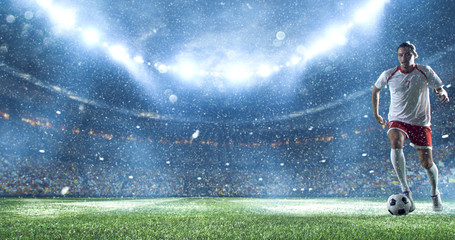 Soccer player kicks the ball on the soccer stadium. He wear unbranded sports clothes. Stadium and...