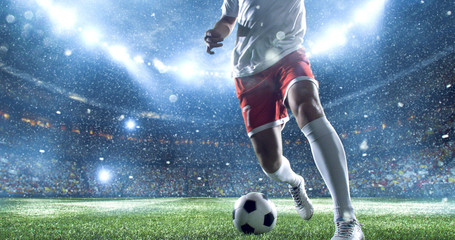 Soccer player kicks the ball on the soccer stadium. He wear unbranded sports clothes. Stadium and...