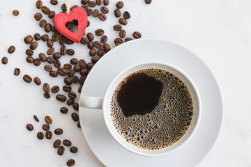 White cup of coffee with coffee beans are scattered around.