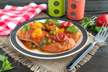 Fish fillet cooked in tomato sauce with green peas and cherry tomatoes on a plate on a wooden background. Healthy eatng concept. Easy cooking.