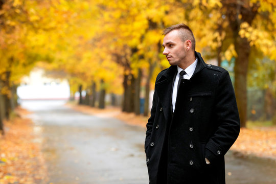 Attractive man in black coat in autumn rainy forest. Free place vor text. Fashion and clothing concept.