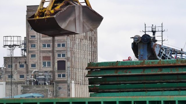 argo ship being loaded with reddish earthy material, derelict building in the background.