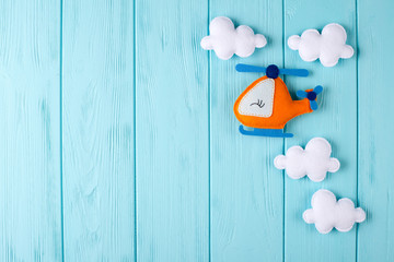Orange craft helicopter and clouds on blue wooden background with copyspace. Felt handmade toys. Empty space for text. Top view.