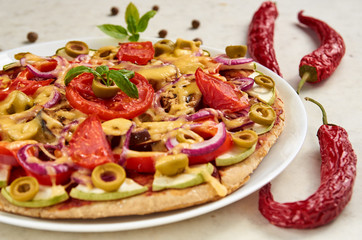 Vegetarian pizza with tomatoes, bell pepper, onion, green olives, cheese and spices on white background close up decorated with fresh basil and three chili peppers. Close up view