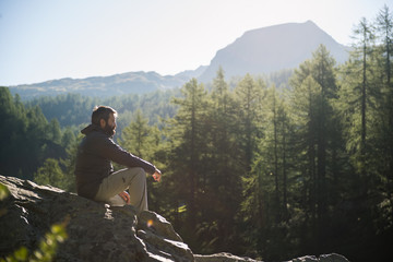 Young adult active man sitting on top rock looking at panorama in sunny spring summer morning on mountain outdoor. - Powered by Adobe
