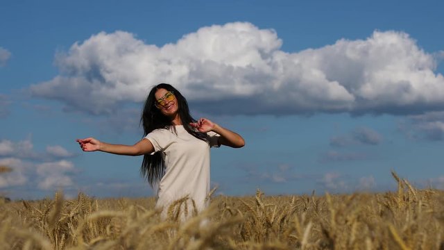 Young brunette in yellow glasses is dancing in a wheat field
