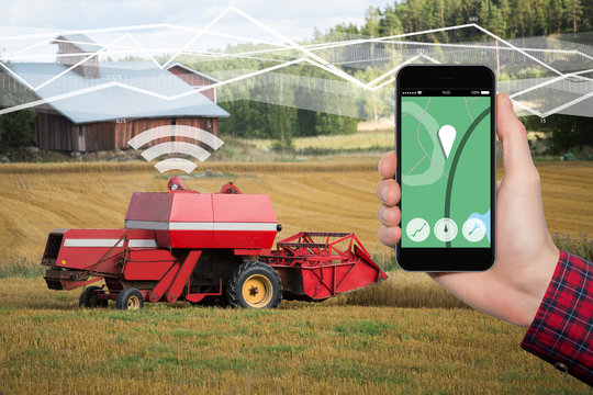 Hand with phone. On the screen control interface of the self driving combine harvester. Internet of things in agriculture