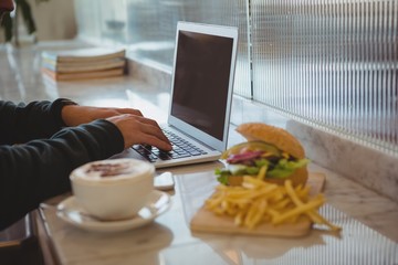 Cropped hands of man using laptop by coffee cup and French fries