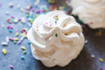 Beautiful italian meringue cookies on dark gray background with colorful sprinkles. Selective focus, close up
