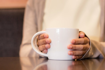 Person hand holding a white cup of coffee with blurry background