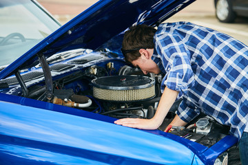 Young man standing at open hood and repairing car