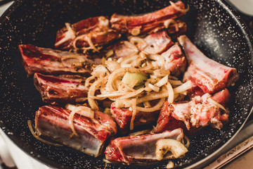 Roasted pork ribs with onion in frying pan, top view