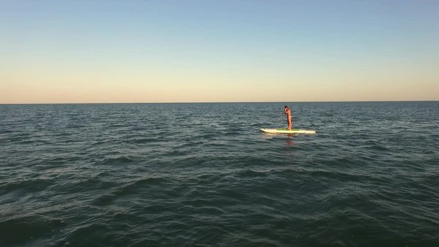 Fit female standing on SUP board in distance, paddling, calm water